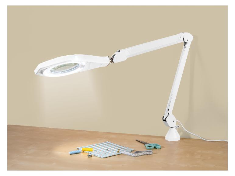 Witte vergrootlamp met naaibenodigdheden op een houten tafel.