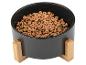 Zwarte voerbak voor huisdieren met een houten standaard, gevuld met droogvoer.