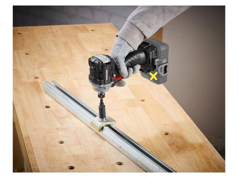 Een gehandschoende hand houdt een snoerloze slagschroevendraaier vast die een schroef in een metalen rail op een houten tafel draait.