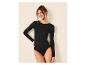 Vrouw in een zwart bodysuit met lange mouwen, lachend en leunend tegen een muur.