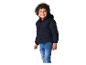 Kleine jongen in een donkerblauwe gewatteerde jas en jeans lachend.