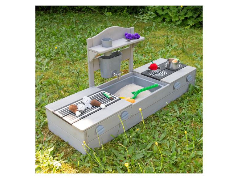 Houten modderkeuken met zand, speelgoedeten en kookgerei in een tuin.