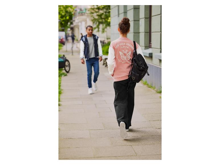 Een vrouw met een roze jas met een vlinderprint loopt op straat met een rugzak.