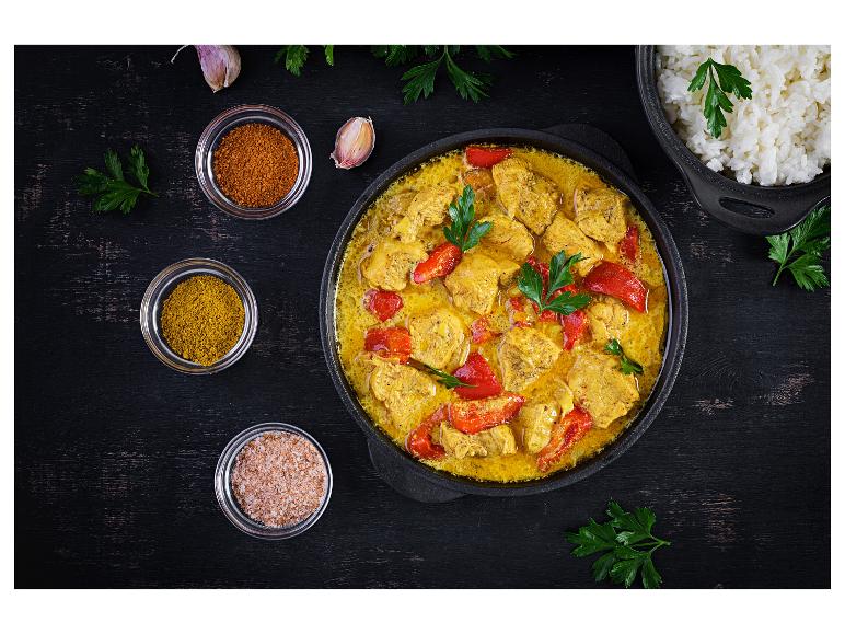 Kipcurry met rode paprika, rijst en kruiden op een donkere houten tafel.