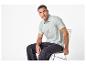 Man in lichtgroen poloshirt en donkere jeans zittend op een stoel.
