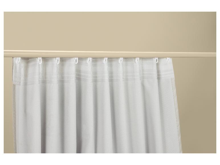 Witte gordijnen met haken aan een gordijnroede tegen een beige muur.