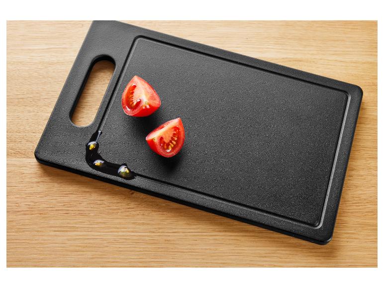 Twee halve cherrytomaten op een zwarte snijplank met olie