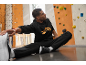 Man in zwarte hoodie en joggingbroek rekt zich uit op de vloer voor een klimmuur.