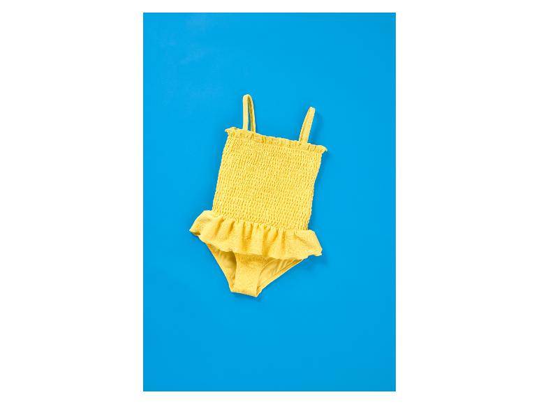 Geel kinderzwempak met ruches op een blauwe achtergrond.