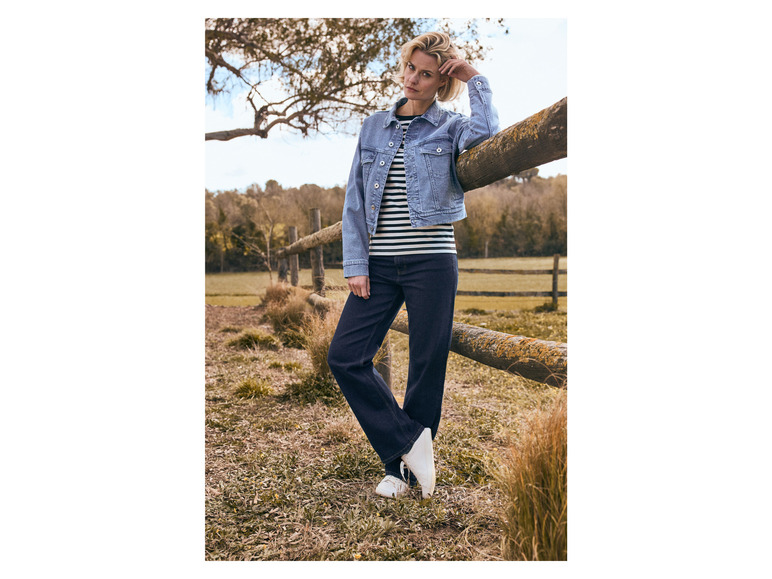 Een vrouw draagt een spijkerjack, gestreept shirt en blauwe jeans.