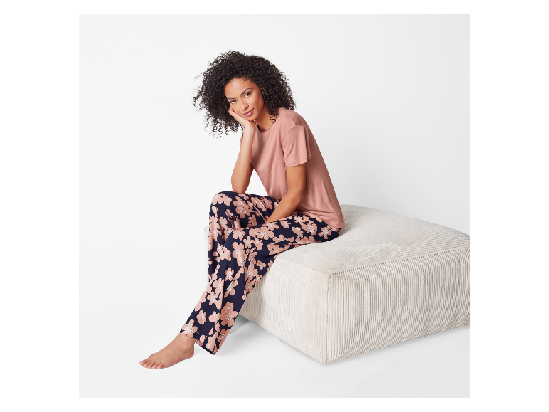 Model in een bloemen pyjama en roze t-shirt zit op een poef.