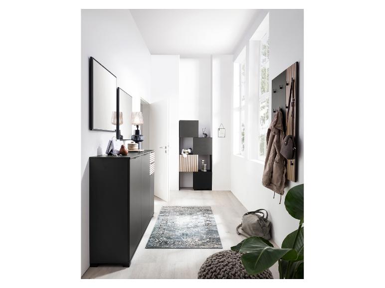 Moderne hal met zwart meubilair, spiegels, kapstok en een vloerkleed met patroon.