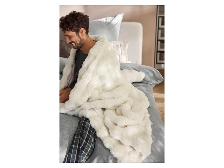 Man in pyjama gewikkeld in een premium LIVARNO® deken op bed.