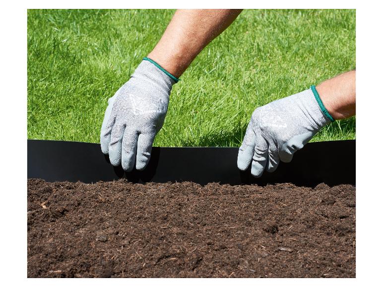 Handen met handschoenen installeren een zwarte tuinafscheiding tussen gras en aarde.