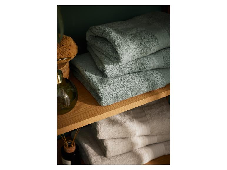 Stapel zachte saliegroene badhanddoeken op een houten plank, naast andere beige handdoeken.