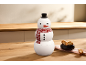 Sneeuwpop koekjespot met hoed en sjaal, naast een schaal met koekjes op een houten tafel.