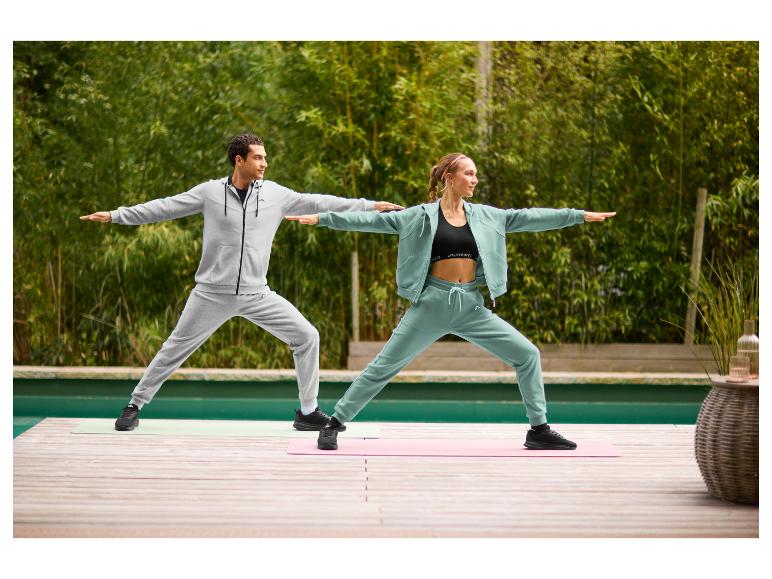 Een vrouw in een saliegroen CRIVIT sweatvest en bijpassende joggingbroek doet buiten aan yoga.