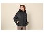 Vrouw in zwarte pufferjas met capuchon en bruine broek, handen in zakken.