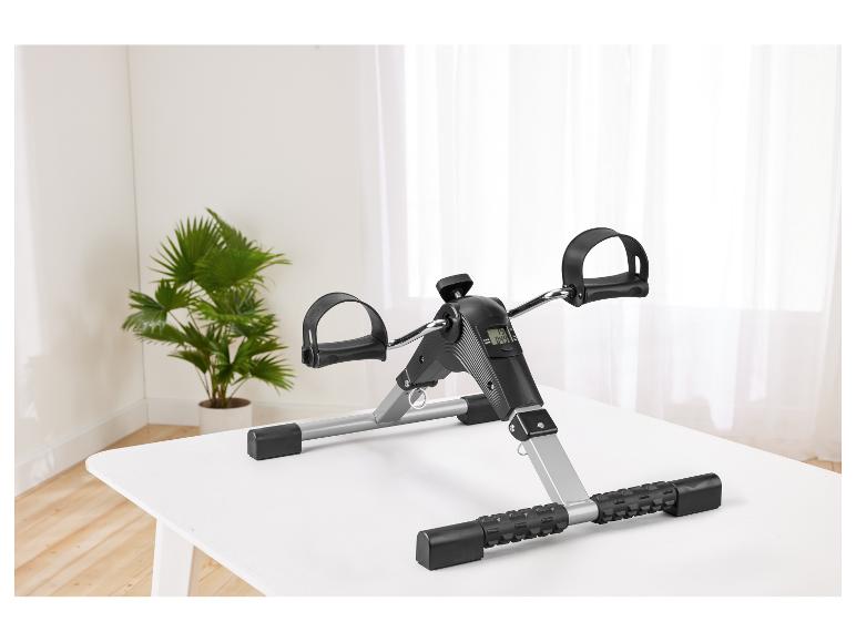 Mini hometrainer met digitaal display op een witte tafel, met een plant op de achtergrond.