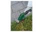 Accu grastrimmer die gras langs een stenen pad maait.