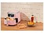 Roze airfryer met friet, ketchup en zout op een houten aanrecht.