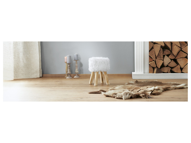 Een wit pluche poefje met houten poten, een bruin bontkleed en drie kandelaars.