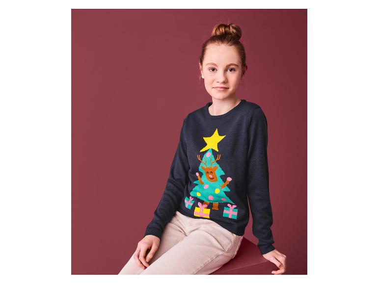 Een meisje draagt een kersttrui met een rendier in een kerstboom.