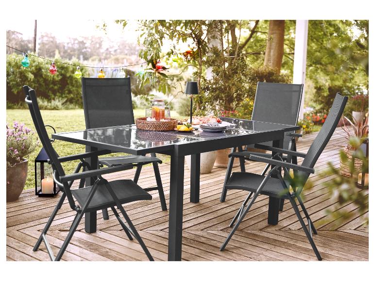 Buiten eethoek met glazen tafel en vier donkergrijze klapstoelen op een houten terras.