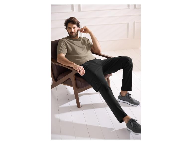 Man in een beige T-shirt en zwarte broek zit in een fauteuil.