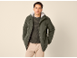 Man in groene parka met capuchon, donkergroene trui en beige broek.