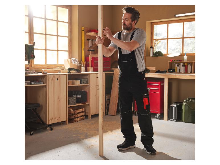 Een man in Parkside werkkleding meet een stuk hout in zijn goed uitgeruste werkplaats.