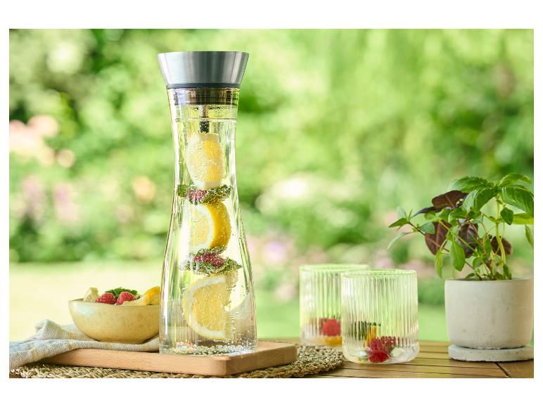 Waterkan, glazen en vers fruit op een buitentafel.