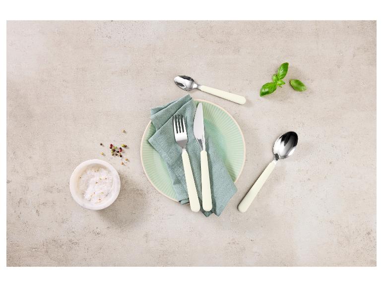 Bestekset met bord, servet, zout, peper en basilicum op een lichte achtergrond.