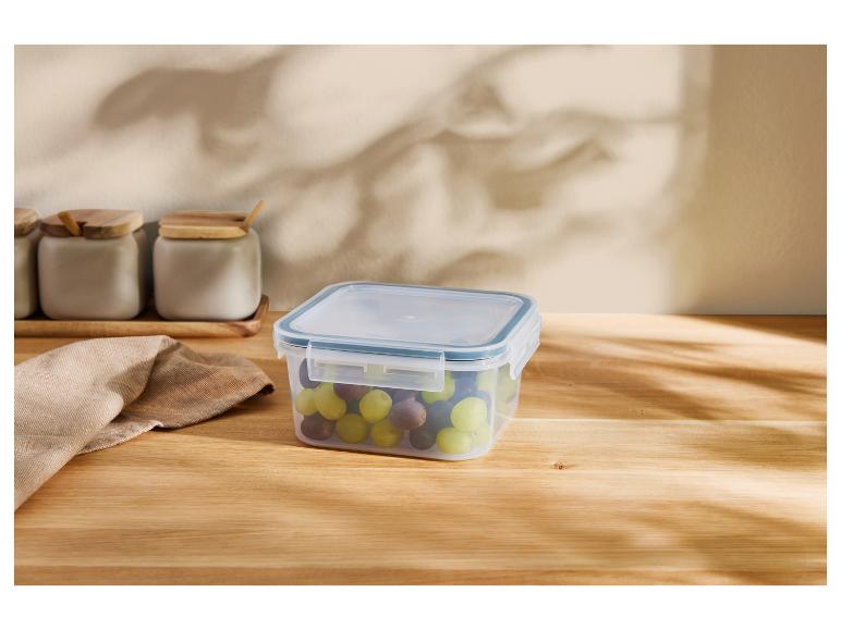 Transparante bak met druiven op een houten tafel, potten op de achtergrond.