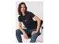 Vrouw in donker T-shirt met opdruk en jeans, zittend op een stoel.