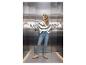 Vrouw in gestreepte trui, jeans en sneakers, poserend in een moderne lift.