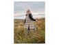 Vrouw in lange, beige gewatteerde bodywarmer en jeans loopt door grasveld.