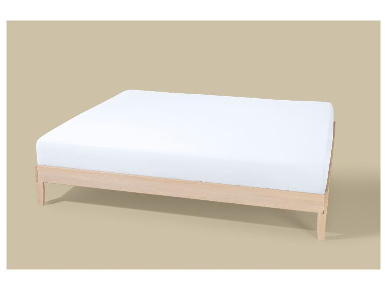 Licht houten bedframe met een wit matras op een beige achtergrond.