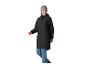 Vrouw in zwarte regenjas, blauwe jeans en grijze muts, lachend en lopend.