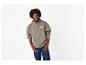 Man in een kaki hoodie met de tekst '23 OUT OF THIS WORLD' en donkerblauwe jeans