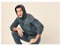 Man in donkergrijs trainingspak, hoodie en joggingbroek, gehurkt.
