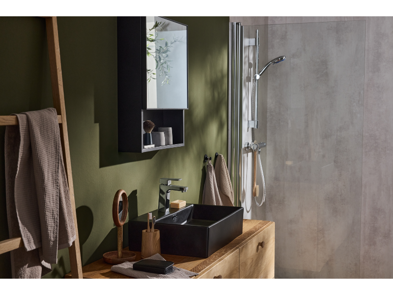 Badkamer met groene muur, zwarte wastafel en douchecabine.