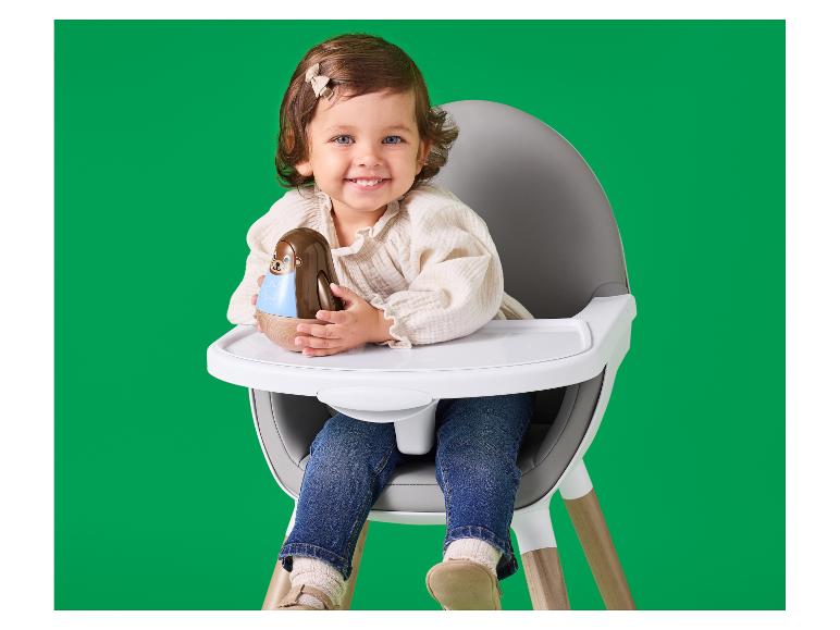 Lachende baby in kinderstoel met een rammelaar.