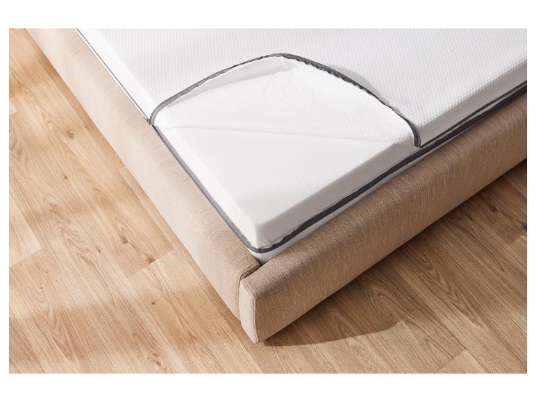 Een schuimmatras op een bed met een gestoffeerde hoofdeinde.