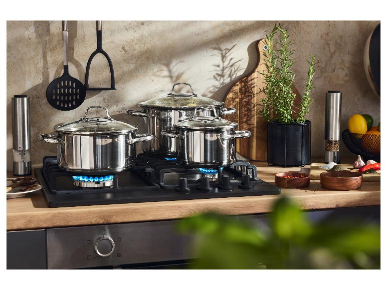 Drie roestvrijstalen pannen op een gasfornuis, met keukengerei en kruiden