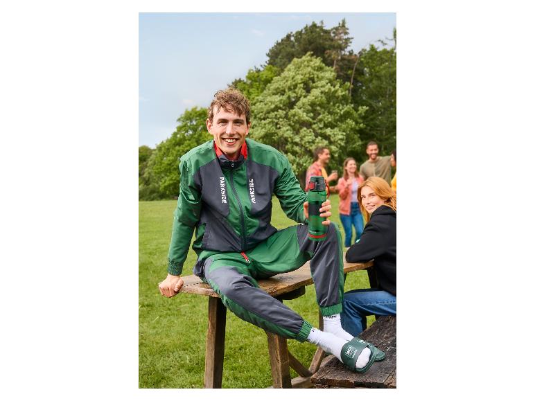 Glimlachende man in een groen-grijs PARKSIDE® jack zit buiten.