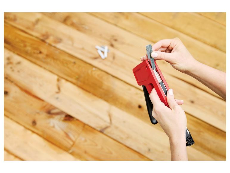 Een persoon laadt een rode LIVARNO® Handtacker »R53 T&F« met nietjes op een houten ondergrond.
