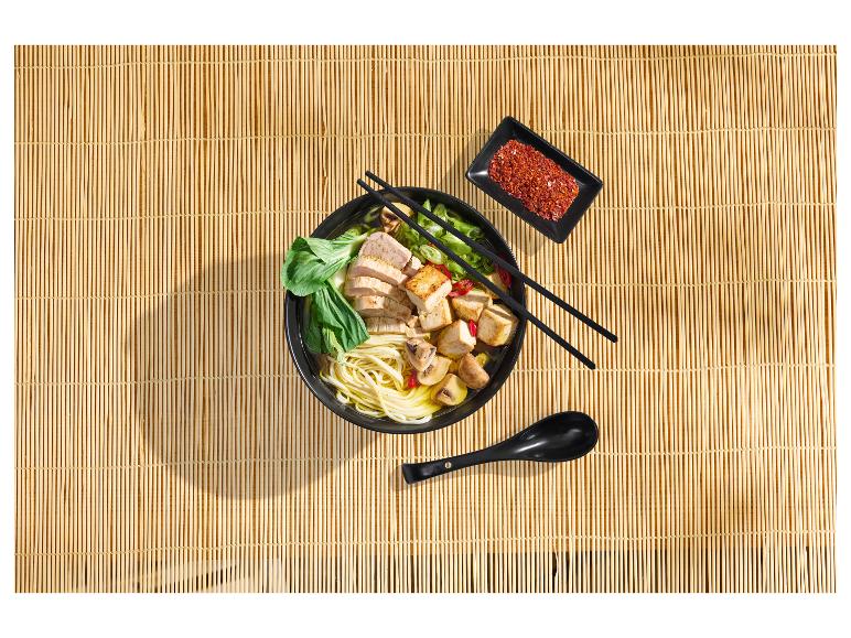 Kom ramen met kip, tofu, champignons en paksoi op een bamboemat.