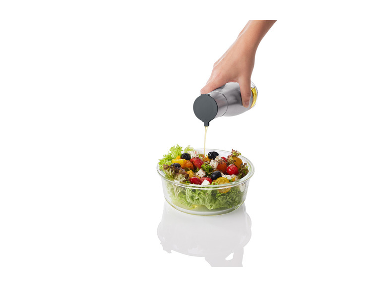 Een hand giet olie uit een fles op een salade in een glazen kom.