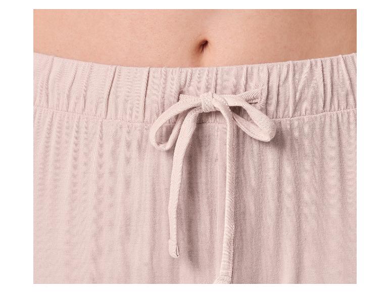 Close-up van de buik van een vrouw in een lichtroze pyjamabroek met trekkoord.